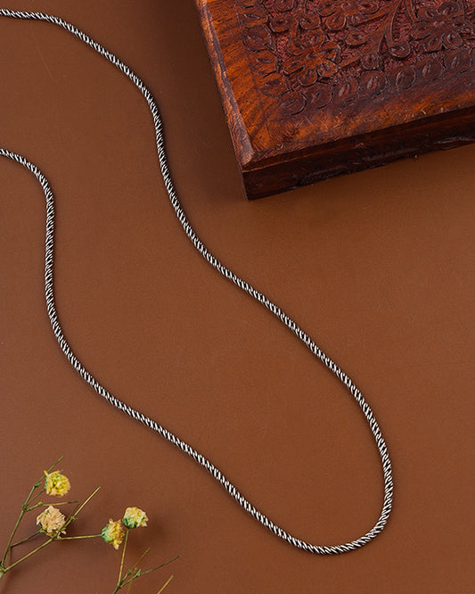 Silver chain necklace on a brown surface with a wooden box and small flowers.