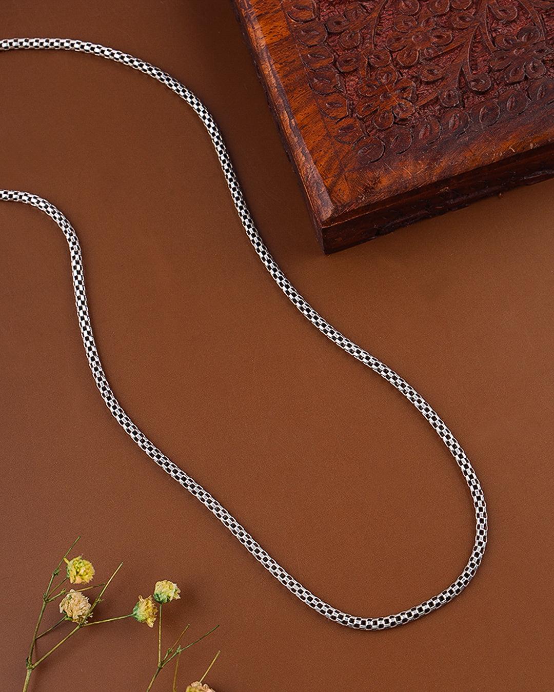 Black and white patterned rope on a brown surface with a wooden block and dried flowers.