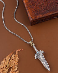 Silver dagger pendant necklace on a brown background with a wooden box and leaf.