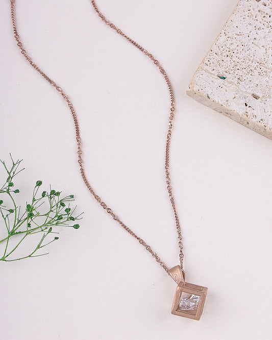 Rose gold necklace with a square pendant on a light surface with greenery