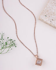 Rose gold necklace with a square pendant on a light surface with greenery