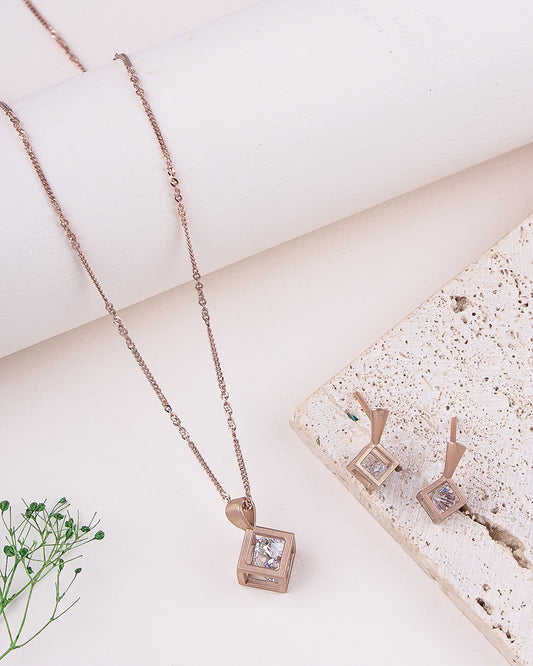 Rose gold necklace and earrings on a textured surface with a light background
