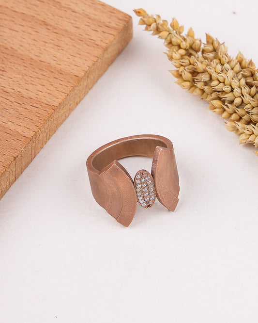 matte rose gold ring with a diamond on a white surface with wooden and wheat elements.