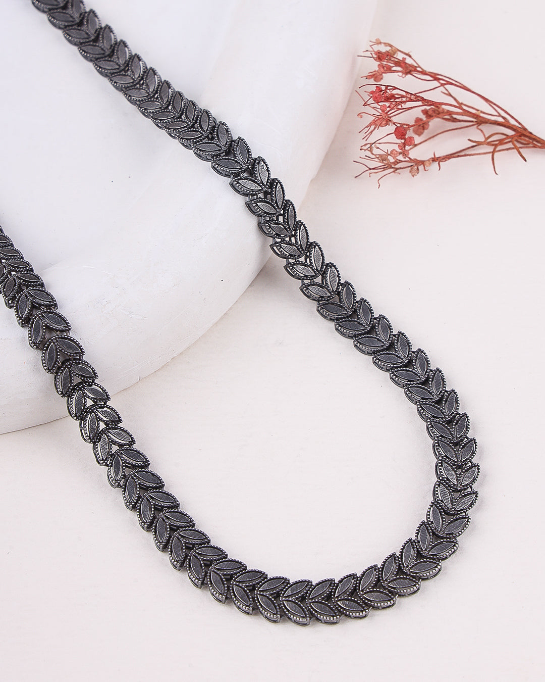 Silver necklace on a white surface with dried flowers in the background