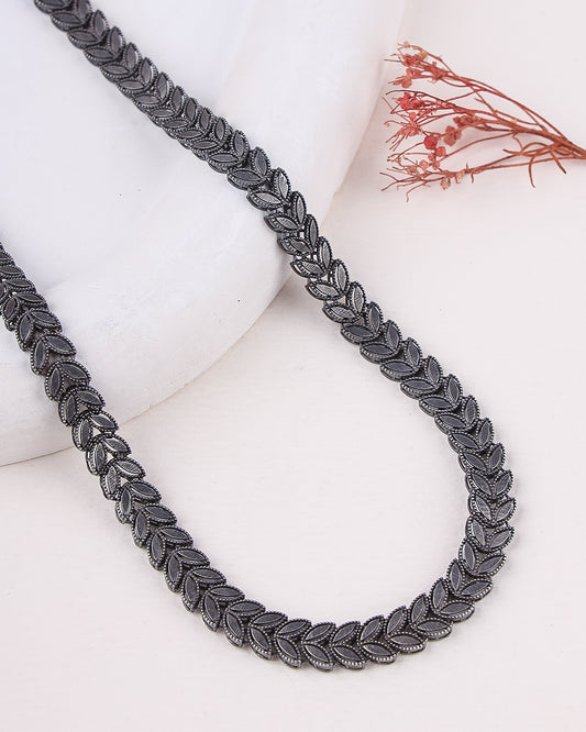 Silver necklace on a white surface with dried flowers in the background