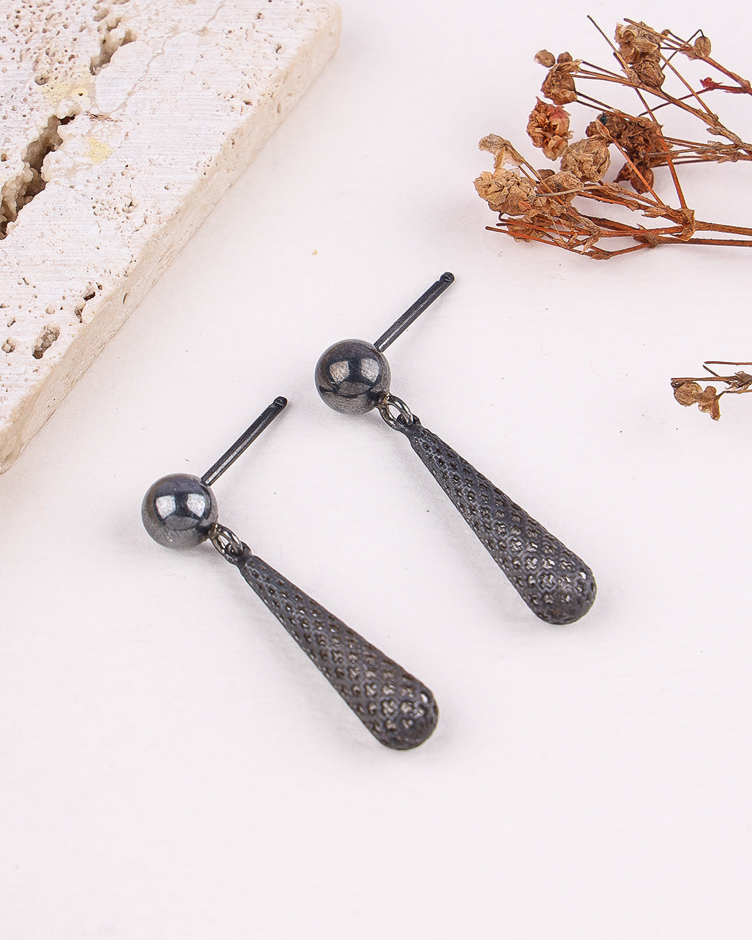 Pair of black teardrop earrings on a light surface with dried flowers.