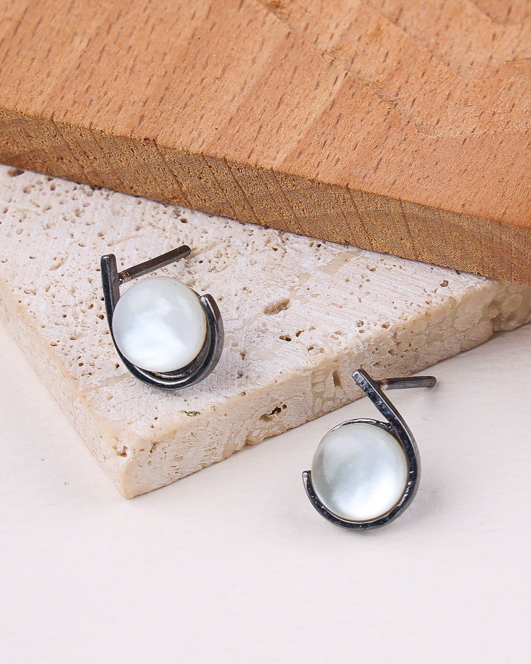 Pair of earrings on a stone surface with a wooden block in the background