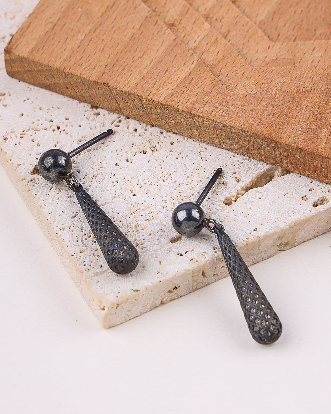 Black earrings on a textured stone surface with a wooden board in the background