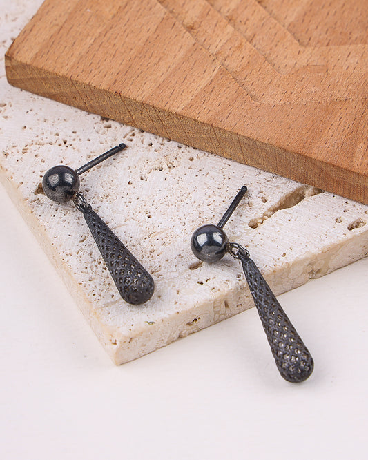 Black earrings on a textured stone surface with a wooden board in the background