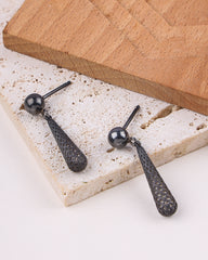 Black earrings on a textured stone surface with a wooden board in the background