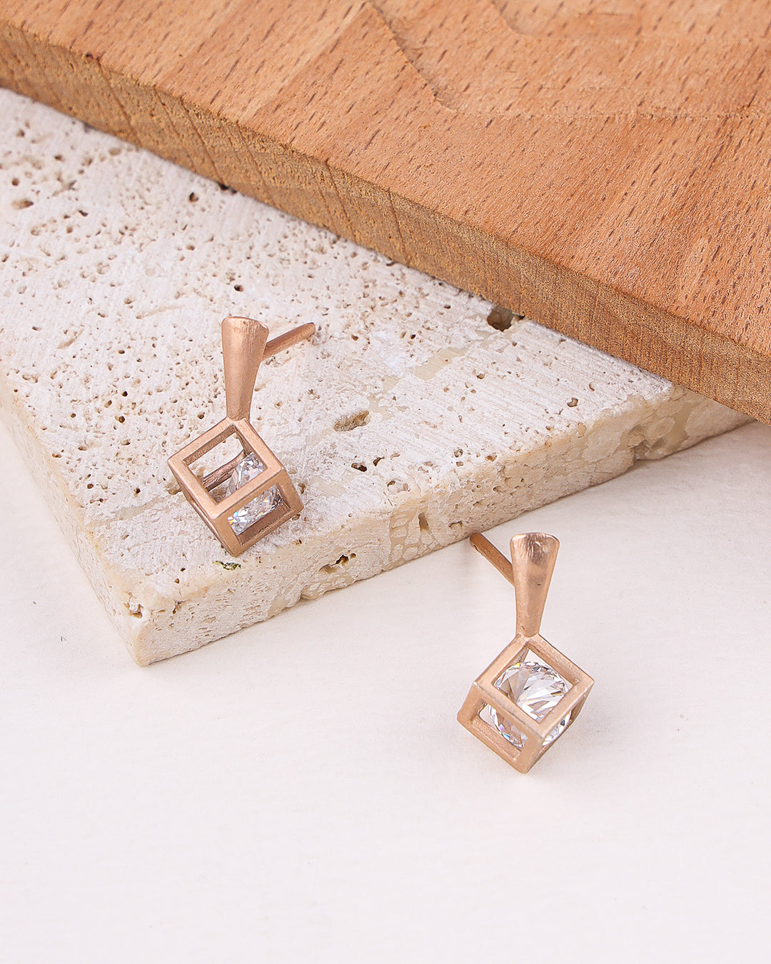 Rose gold earrings with clear gemstones on a textured stone surface.