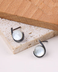 Pair of 925 sterling silver earrings on a stone surface with a wooden block in the background
