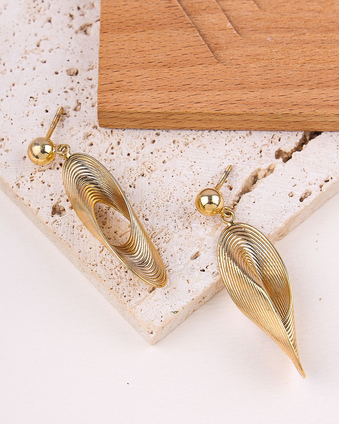 Gold earrings on a textured surface with a wooden block in the background