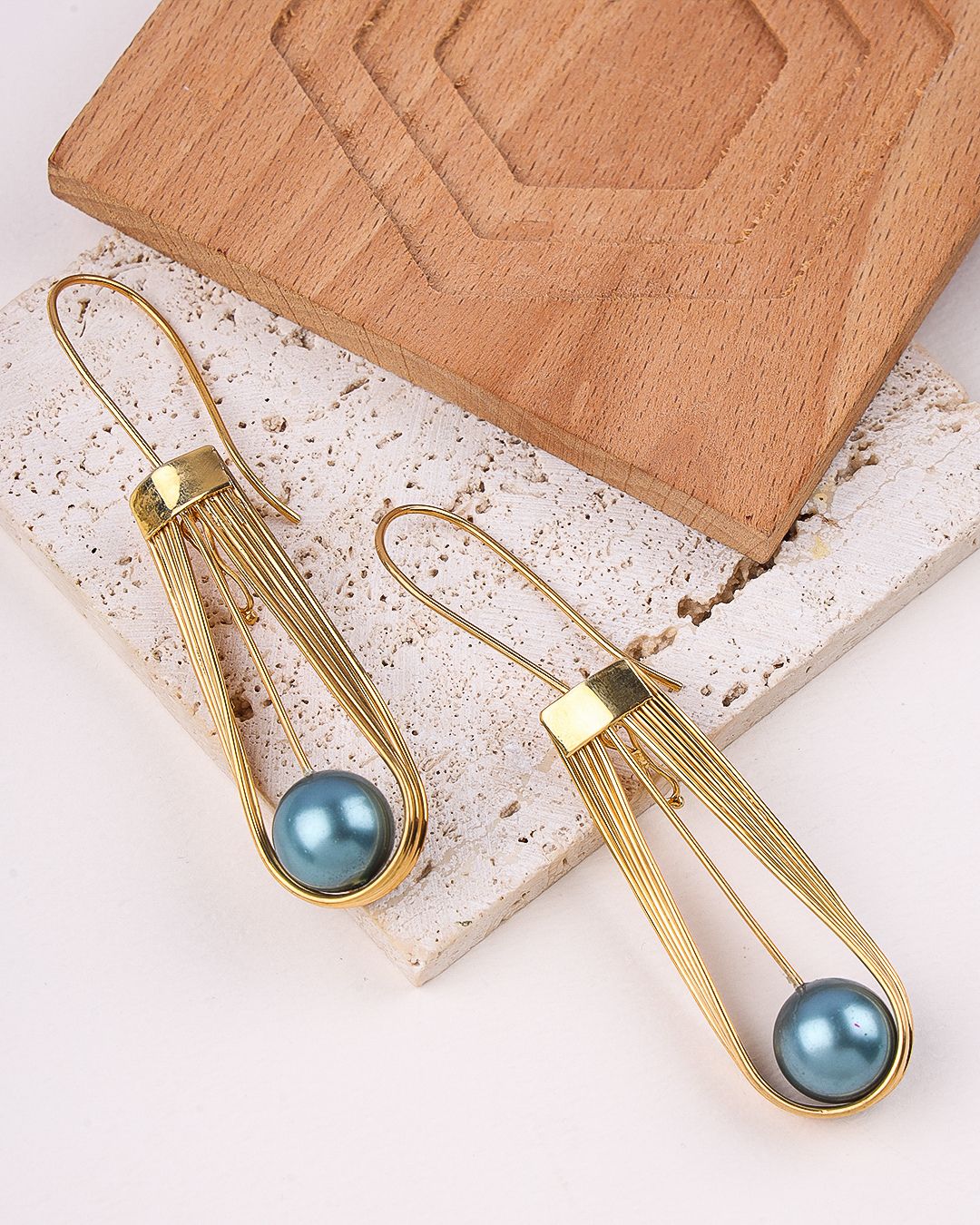 Gold plated earrings with blue spherical beads on a light stone surface.