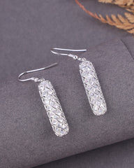 Silver earrings with a textured design on a gray surface
