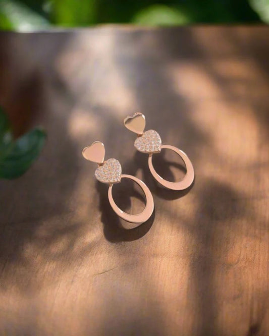 Rose gold earrings with heart and circular designs on a wooden surface