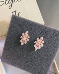 Pair of pink floral earrings on a gray textured surface.