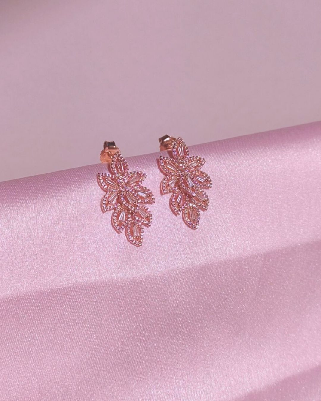 Pair of rose gold earrings on a pink satin surface