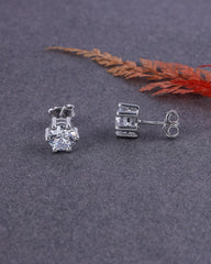 Silver stud earrings on a gray surface with a dried leaf in the background