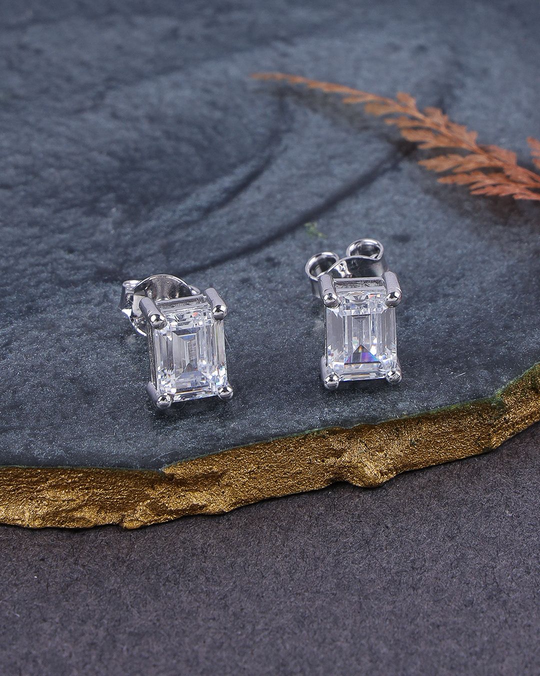 Pair of silver emerald-cut gemstone earrings on a dark stone surface