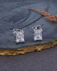 Pair of silver emerald-cut gemstone earrings on a dark stone surface