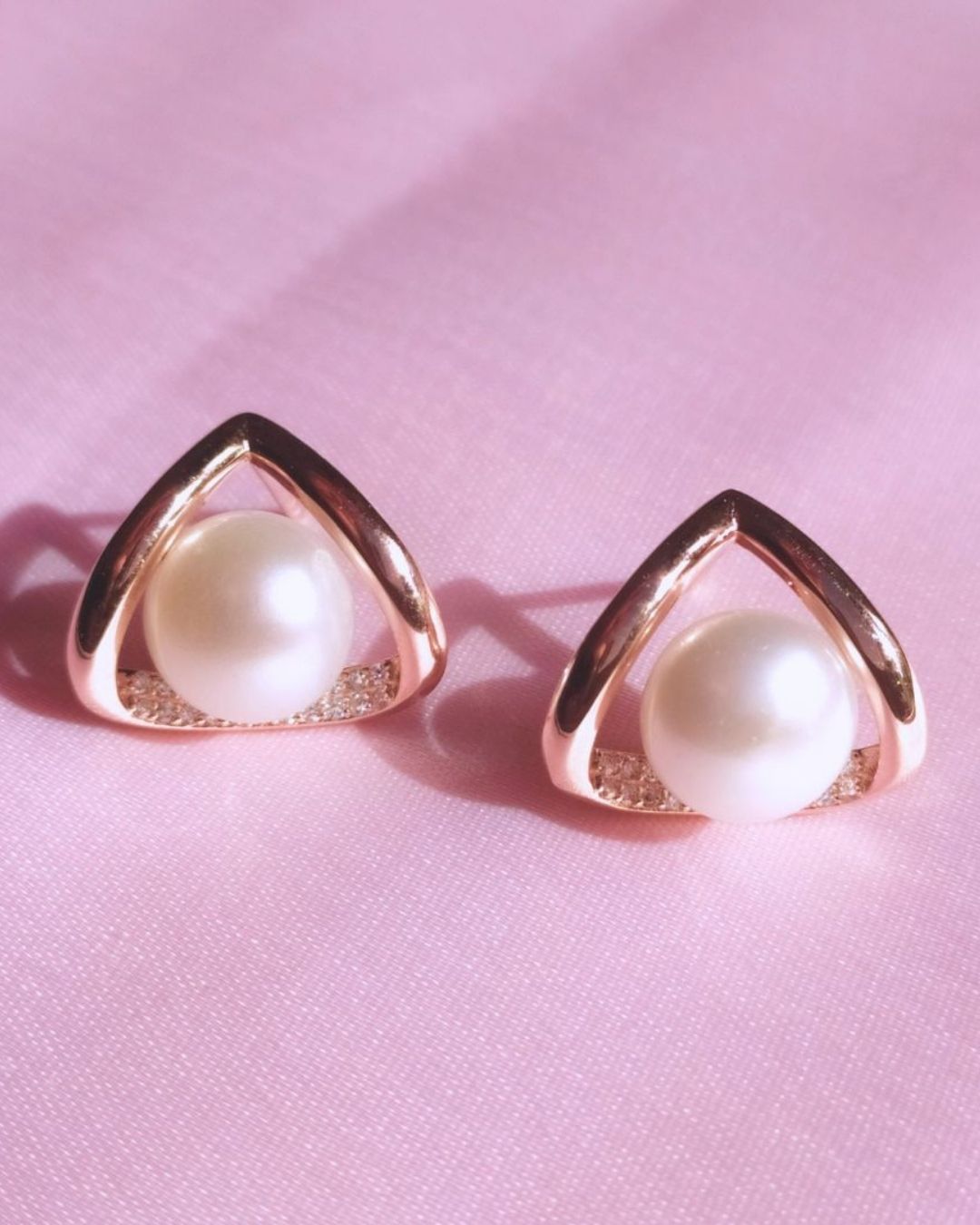 Pair of pearl earrings with gold triangular frames on a pink background