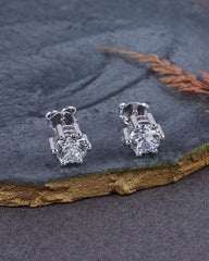 Pair of silver stud earrings with clear gemstones on a textured dark surface.