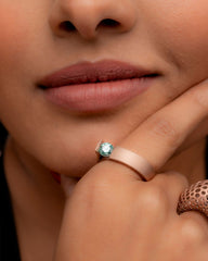 Close-up of a woman's hand wearing a rose gold ring with a blue gemstone.